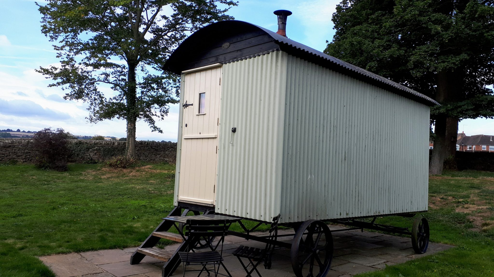 green shepherd hut with three steps and a bistro table and chairs