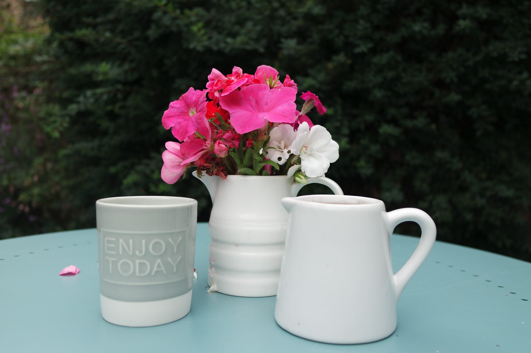 white jug with pink, pelargonium campion and petunia with a jug and a candle enjoy today